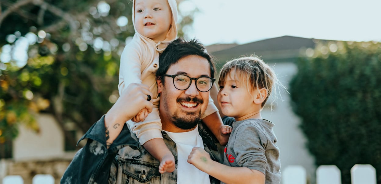 man holding toddler with baby on his shoulders